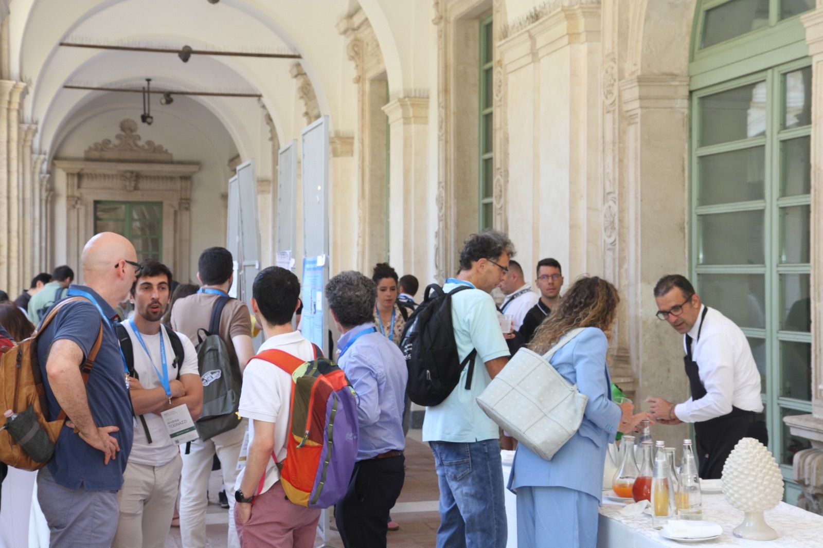 Participants talking around the refreshment tables in the arcaded courtyard during a break at AES 2026