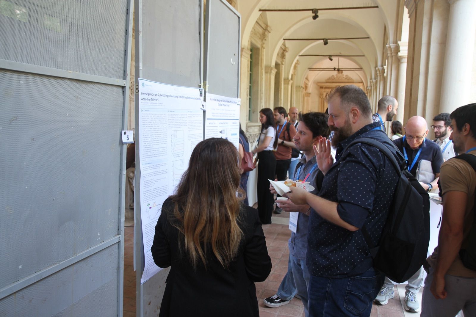 A poster session at AES 2026 in the cloister of the venue: participants reading and discussing the posters