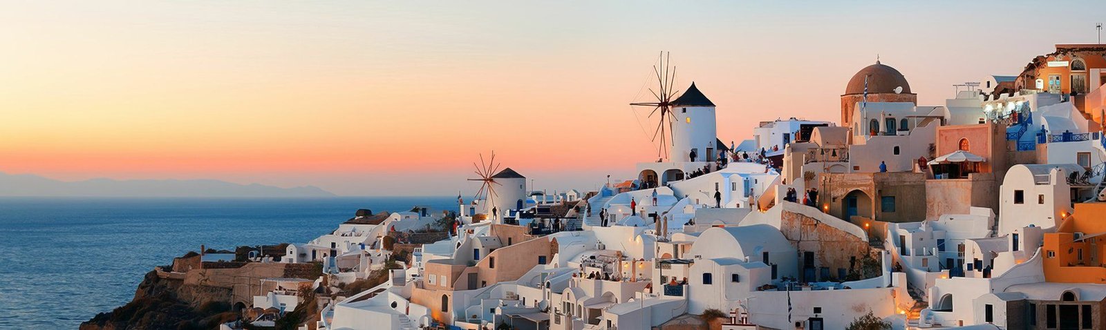 Whitewashed Cycladic houses, windmills and domed churches on a Greek island at sunset, with the sea stretching to the horizon